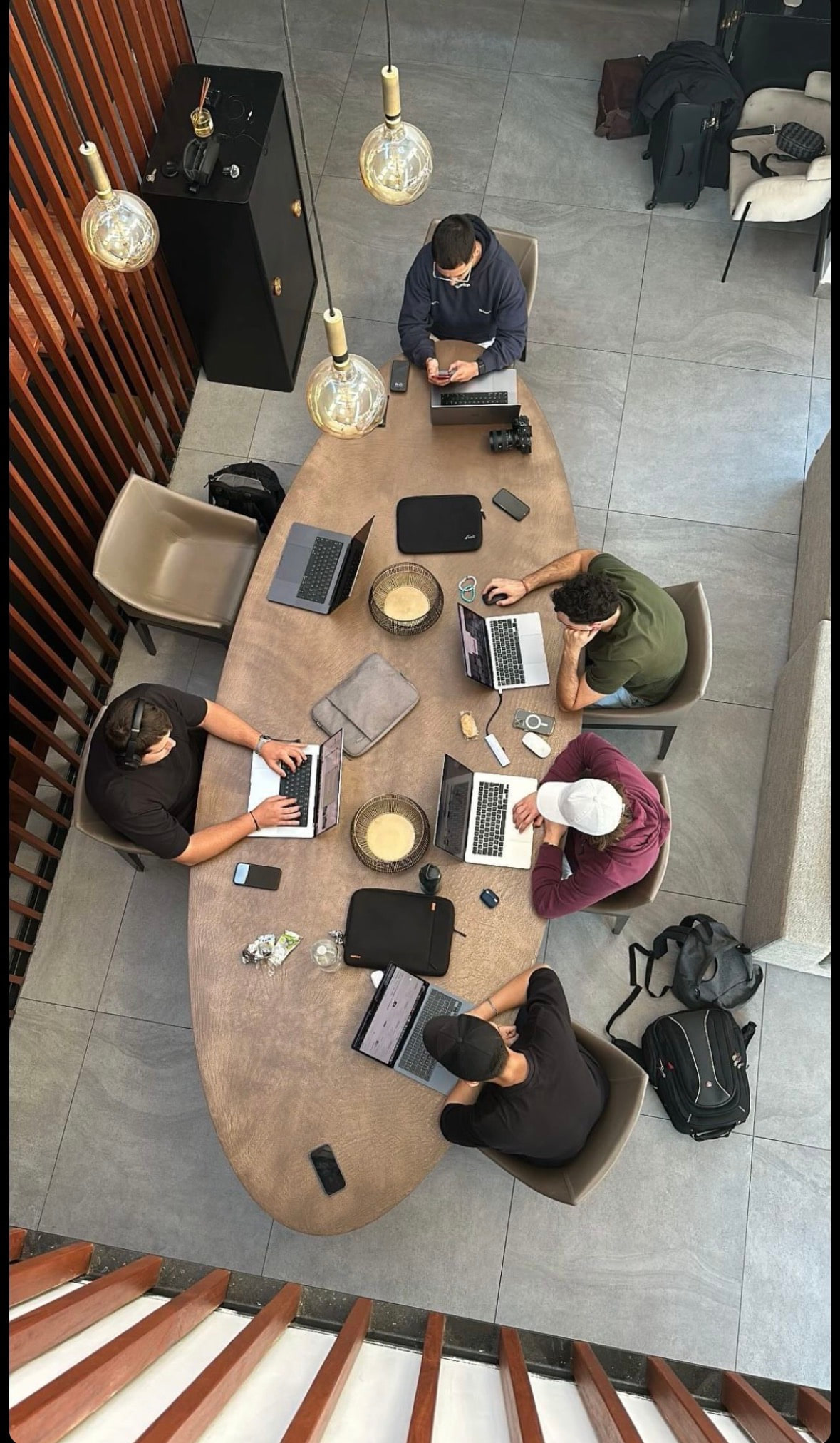 Overhead view of five people working on laptops around a long shared table.