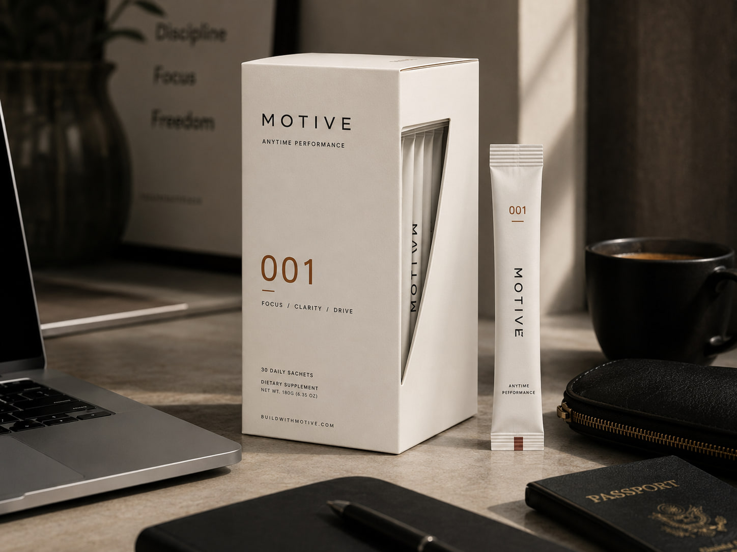 Motive 001 box and a single sachet on a desk in warm afternoon light, beside a laptop, notebook and coffee cup.